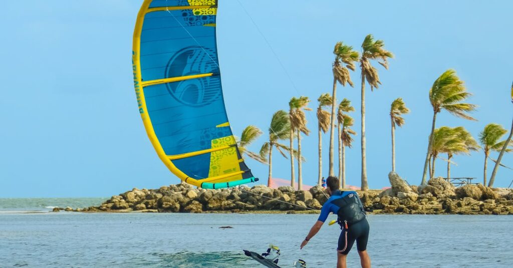 Man enjoying kiteboarding on a tropical beach with palm trees and clear blue water.